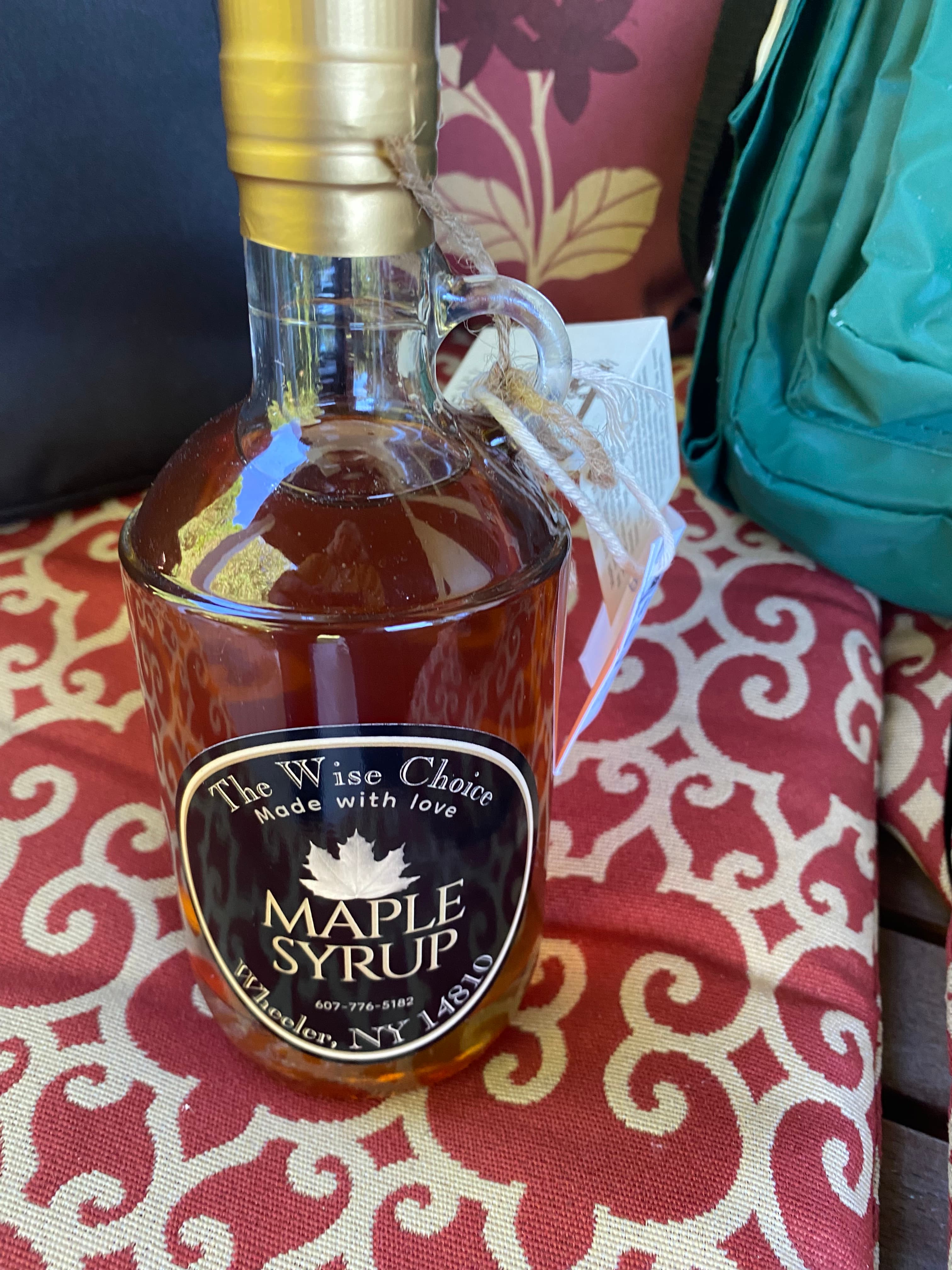 A bottle of maple syrup labeled "The Wise Choice, made with love" resting on a patterned surface.