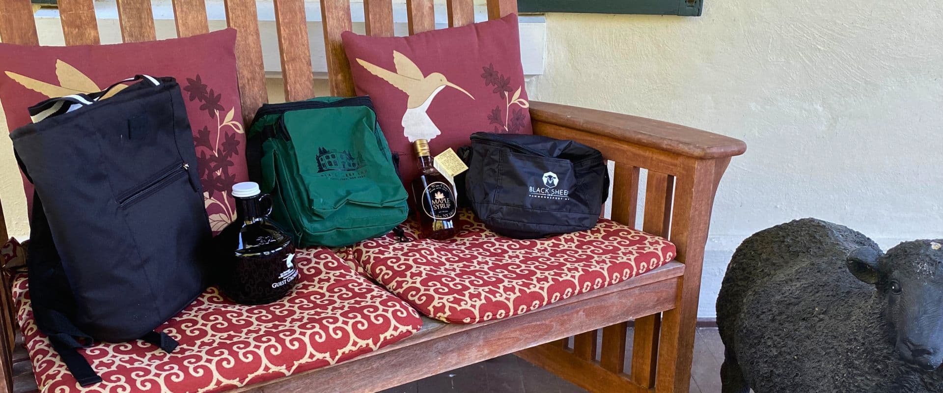 Black and green bags and bottles of beverage neatly arranged on a wooden bench with decorative cushions.