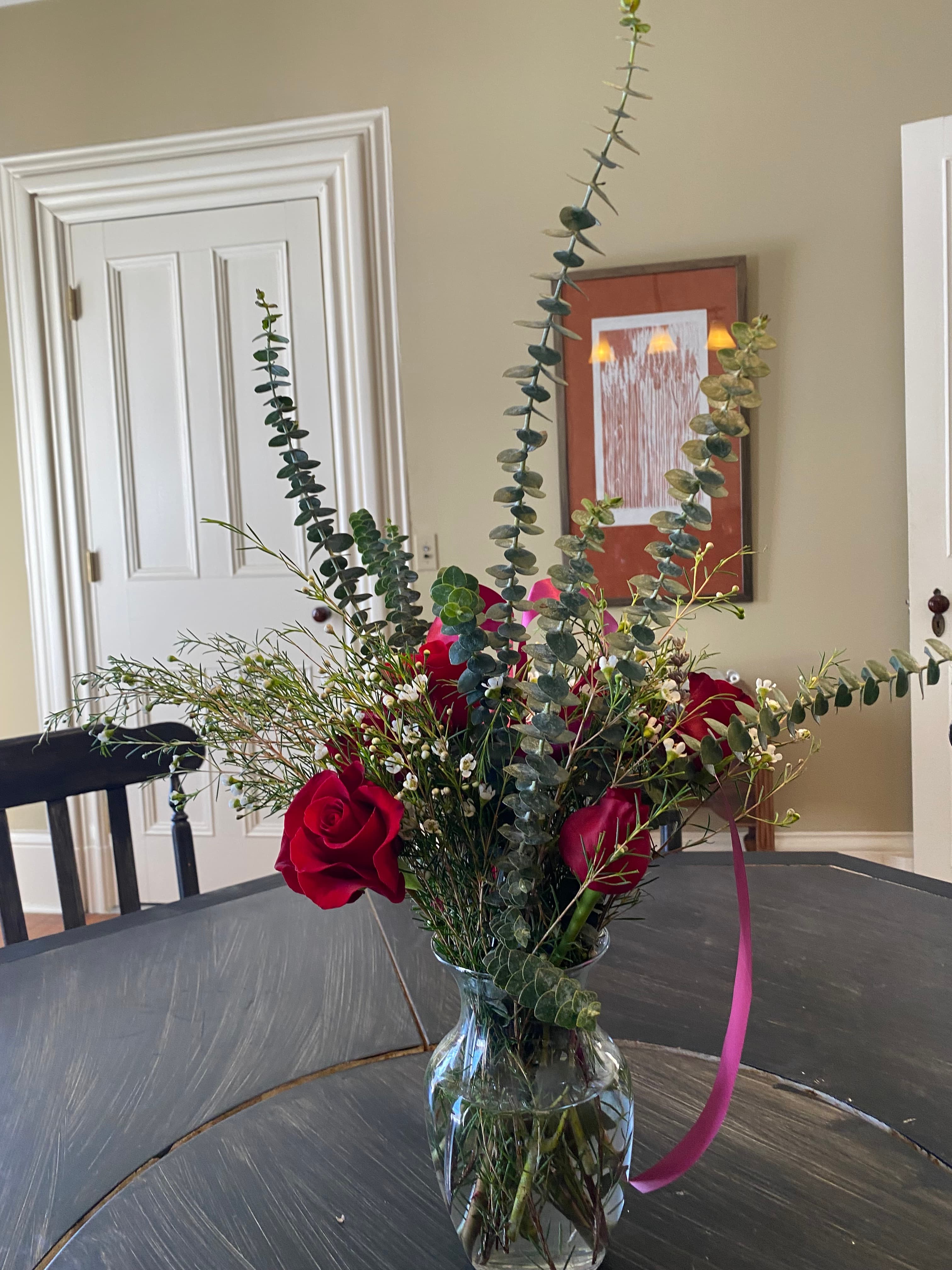 A bouquet of red roses and greenery in a glass vase on a wooden table.