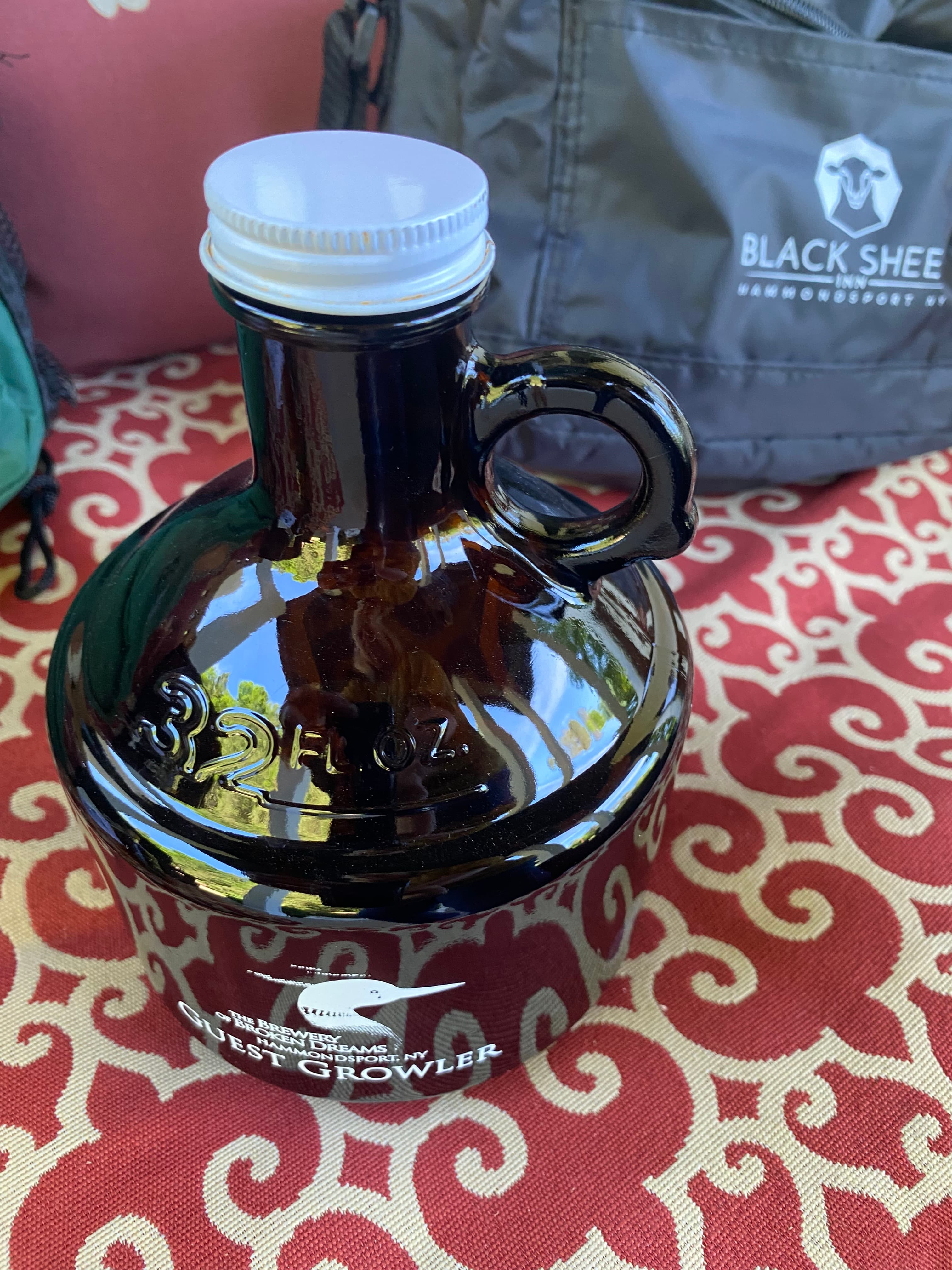 A brown glass growler with a white cap, sitting on a patterned surface.