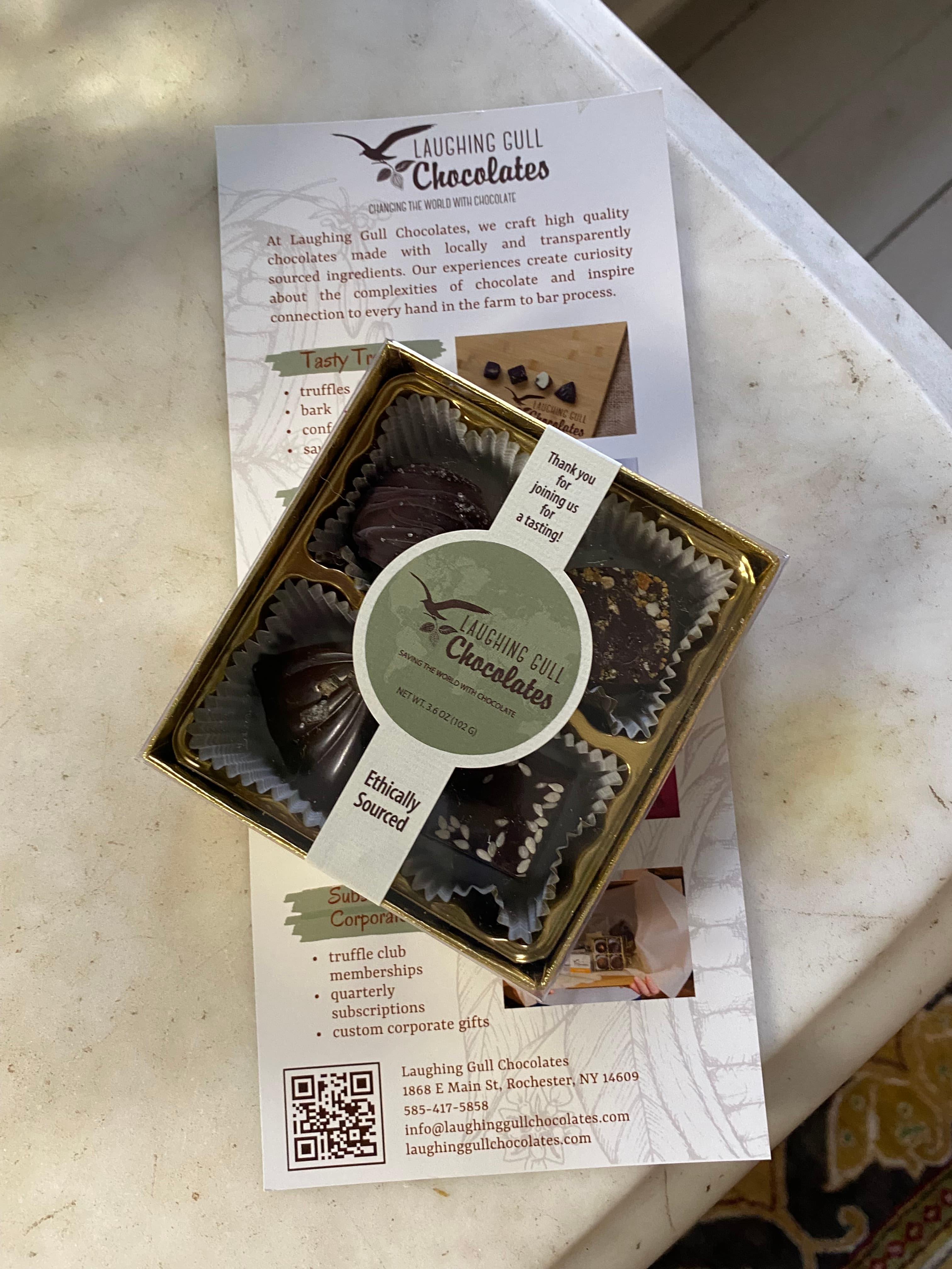 A box of assorted gourmet chocolates sits on a brochure for Laughing Gull Chocolates.