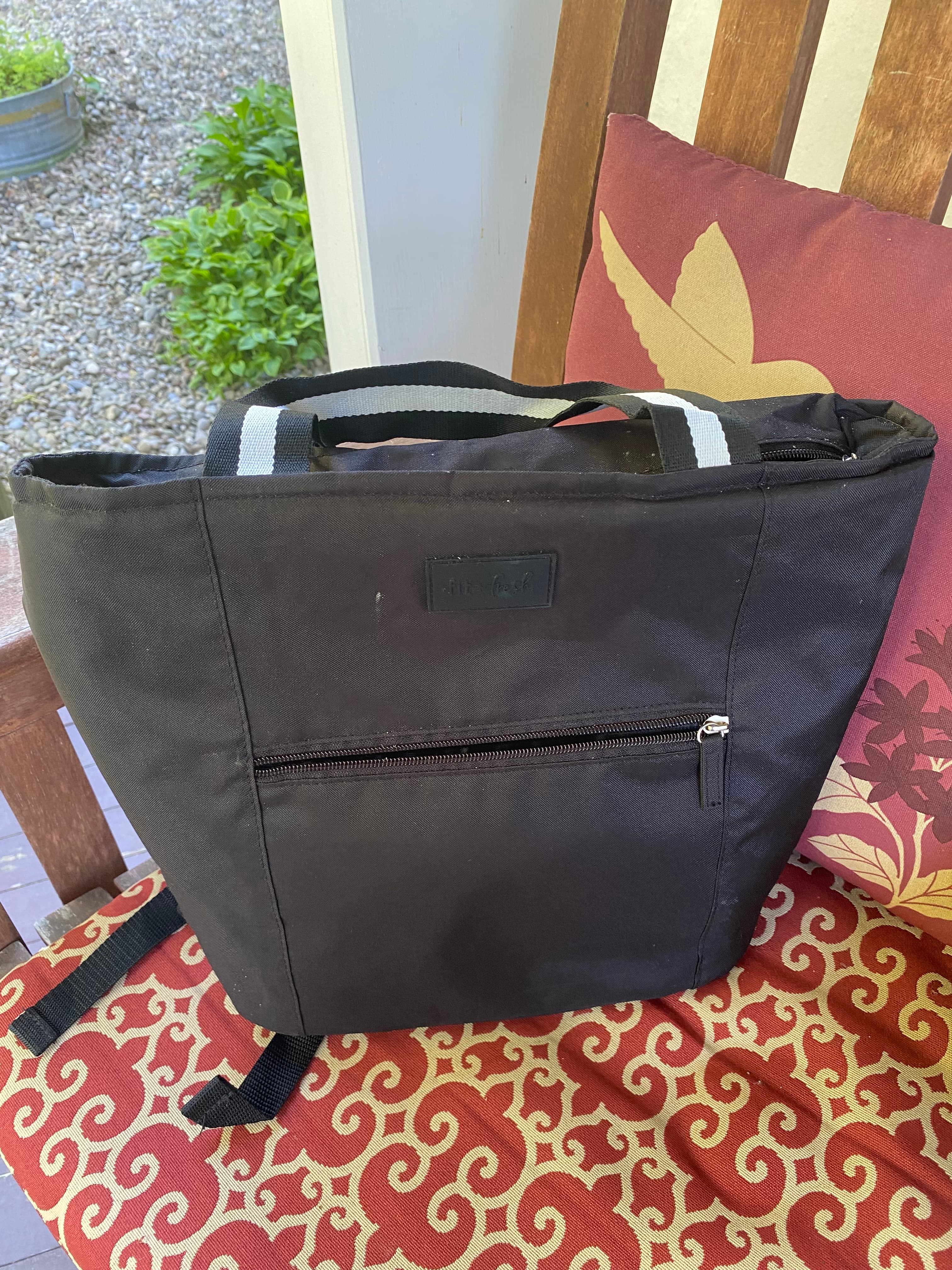 A black tote bag sits on a patterned chair outdoors.