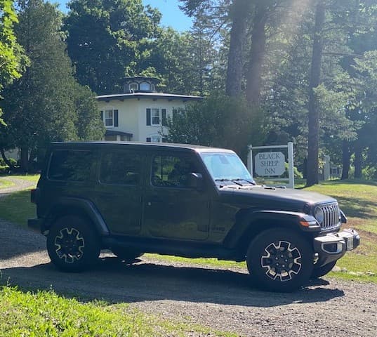 A black SUV is parked in front of the Black Sheep Inn amidst trees and a sunny backdrop.