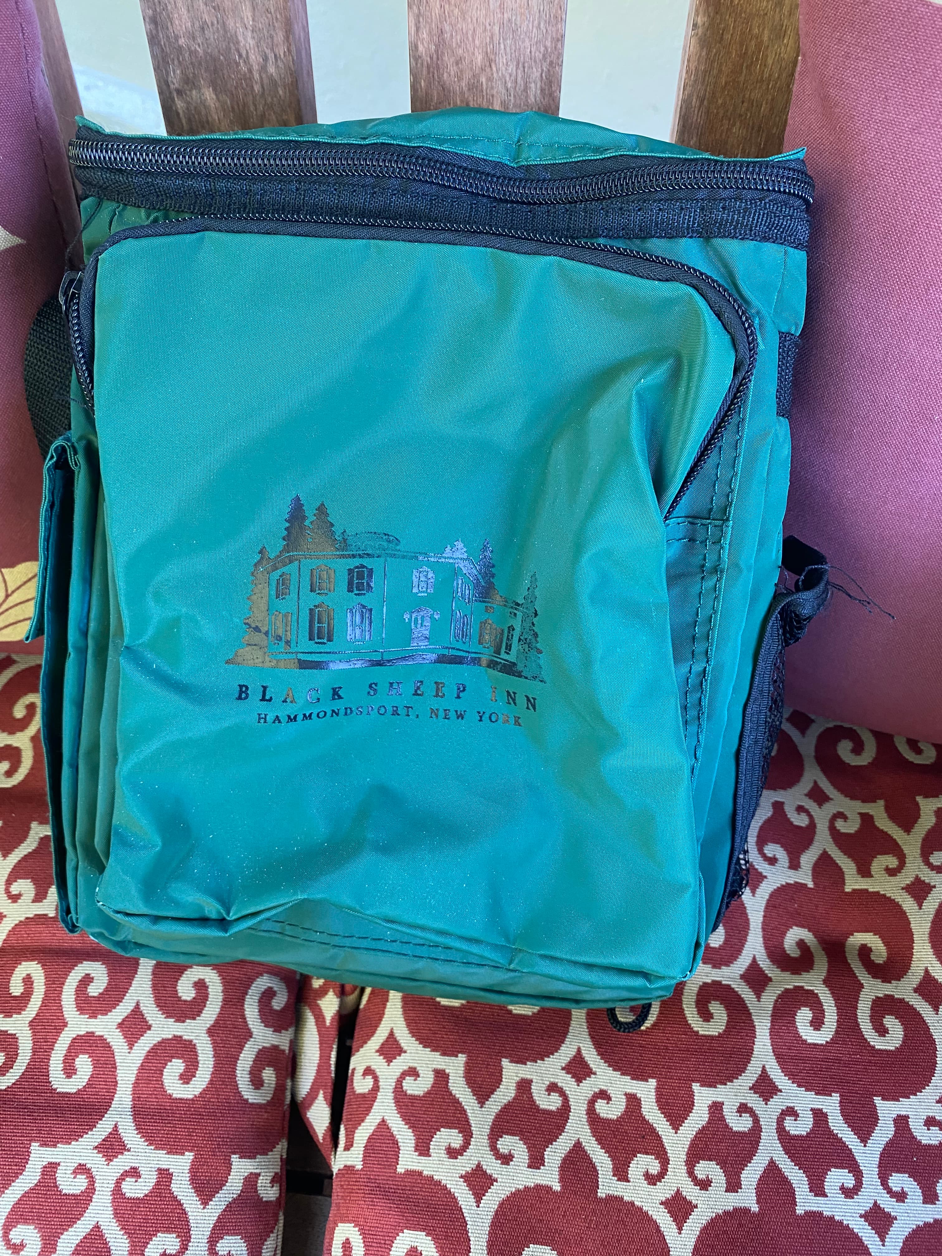 A green bag featuring a logo of the Black Sleep Inn from Hammondsport, New York, resting on a patterned cushion.