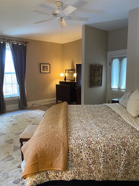 Cozy bedroom with a floral-patterned bedspread, a dresser, and large windows.